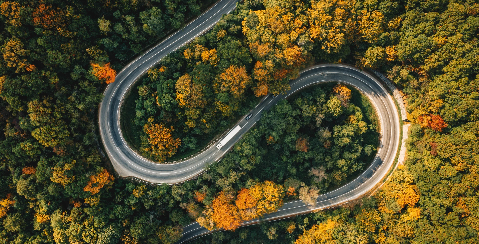 Widok z lotu ptaka na kontrolowaną autostradę wijącą się przez bujny las wiekowy w przełęczy górskiej. Zdjęcie przedstawiające malowniczą leśną drogę.