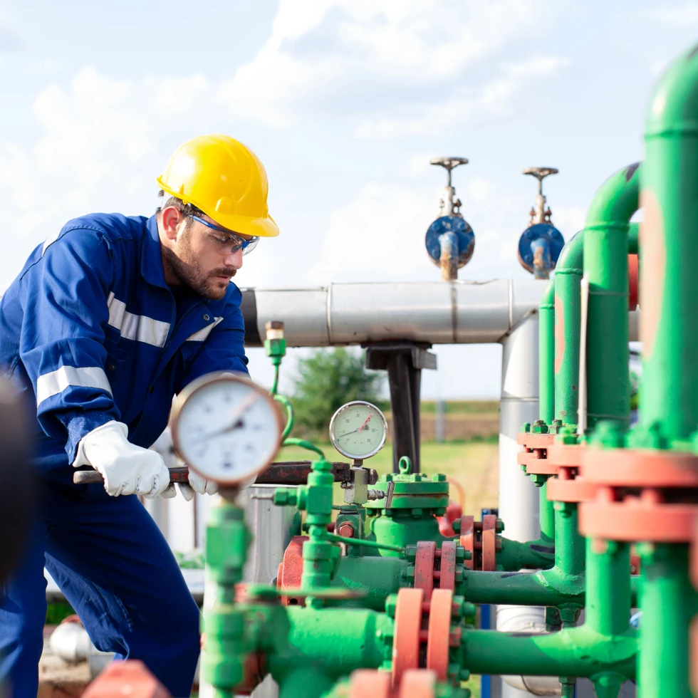 Robotnik fizyczny noszący odzież roboczą i kask ochronny, sprawdzający rurę w ustawieniu przemysłowym. Inżynier przeprowadza prace hydrauliczne na cylindrze, demonstrując swoją wiedzę i doświadczenie w branży.