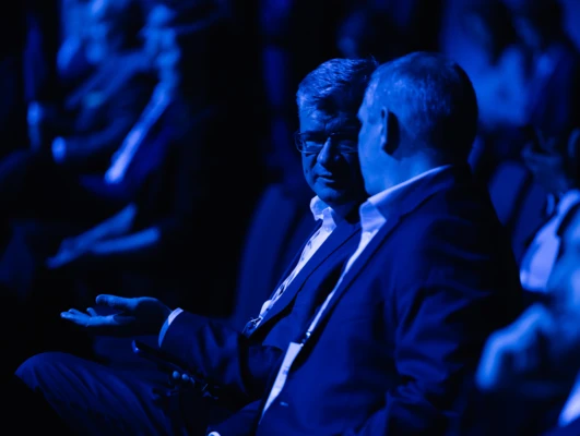 A group of people in formal wear attending a public event. Blue blazers and dress shirts can be seen among the audience.