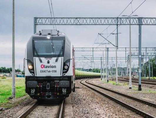 Obraz nowej lokomotywy Olavion E6ACTab-056 na torach kolejowych, środek transportu wykorzystujący tabor. Ten żelazny potwór o mocy 1350 kN jest gotowy do efektywnego świadczenia usług transportu publicznego.