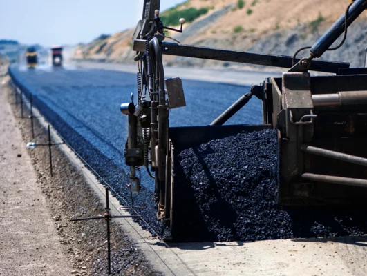 Duża maszyna układająca świeżą asfalt na nawierzchni drogi. Zasadniczy sprzęt ciężki do budowy materiałów takich jak beton i żwir na autostradzie.