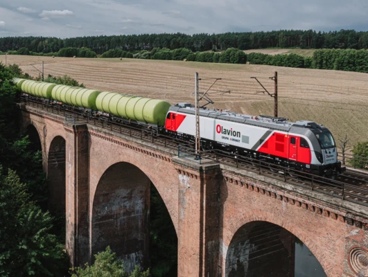 Pociąg z lokomotywą elektryczną i wagonami na torze. Logo GRUPA & UNIMOT znajduje się na boku wagonu kolejowego. Olavion ESACT056.